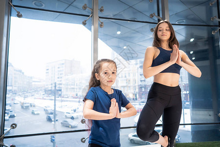 年轻成年母亲和小女儿一起在健身房练瑜伽背景图片