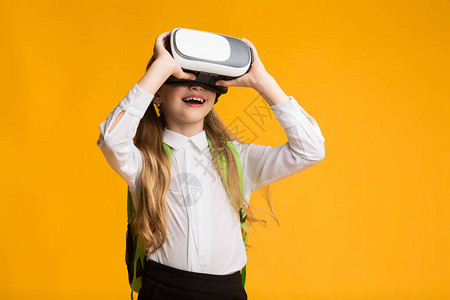 教育未来兴奋的女学生使用VR耳机在黄色背景上体验虚拟现图片