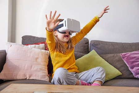 坐在棕色沙发上在家看虚拟现实头戴眼镜的六岁小孩图片