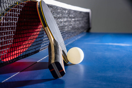 特写黑色和红色乒乓球拍在蓝色乒乓球台上用网拍一个白球图片