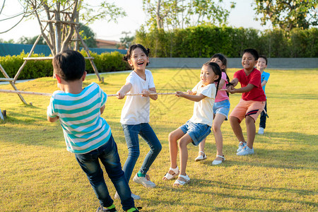 一群快乐的亚裔儿童在夏季天到城区公园操场玩拖战或拉绳牵引器图片