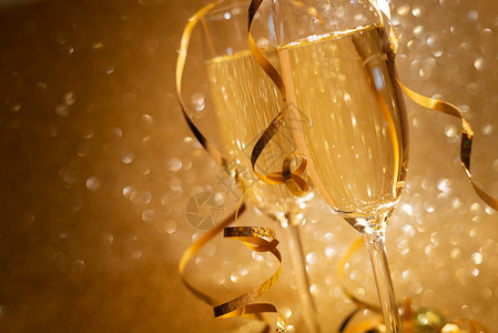 两杯香槟装饰的龙卷风放在金色闪亮背景上圣诞和假期概念图片