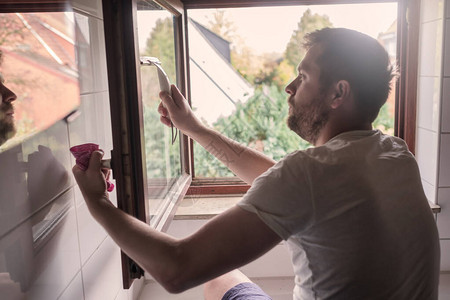 白人男子用刮刀在房子里洗窗户图片