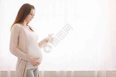 健康营养和怀孕年轻孕妇喝着一杯新鲜牛奶图片