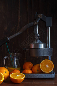 橘子和橘子切片的柑橘和果皮带果汁和柑橘压榨机的玻璃壶在深图片