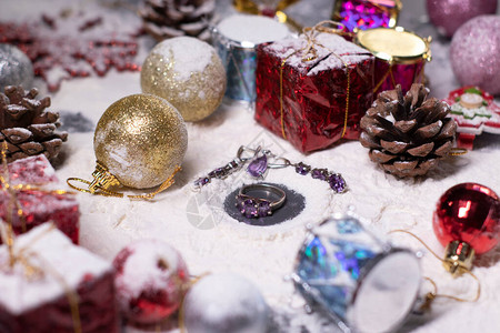 紫色首饰戒指和耳环旁边是雪中的新年装饰品圣诞树球雪花礼物球果圣诞气氛图片