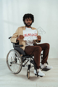 非洲残疾人美国人在看带有标牌的照相机时用白色轮椅写着失业图片