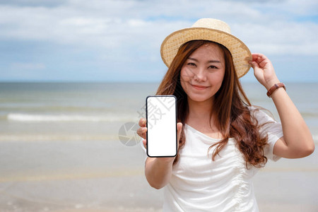 一名妇女站在海滩上时持有和显示黑色手机空白桌面屏幕的黑手图片