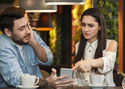 不忠的概念嫉妒的女朋友指着作弊的男朋友电话要求解释坐在自助餐厅图片