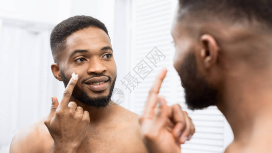 微笑的Afro男人在浴室脸上涂奶油图片