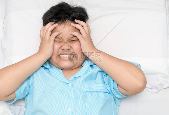 生病的胖男孩在床上头痛顶视高偏头痛或图片