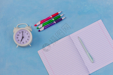 蓝画背景上的已裁定的笔记本笔和时钟顶视图图片