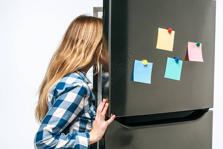 女人看着开的冰箱上面贴着粘黏纸条的女人图片