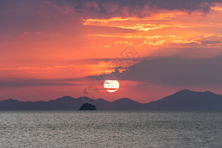 美丽如画的海上日落大红色的太阳圈在海平面上方的山脉和云层的背景图片