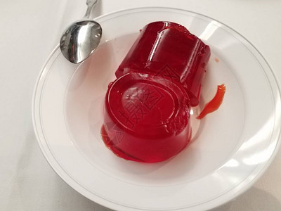 白色碗里的红色明胶甜点桌上放着勺子图片