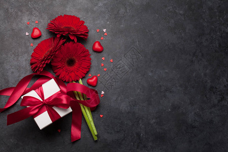手拿礼物盒情人节贺卡与非洲菊鲜花束和礼品盒在石头背景与空间为您的问候背景