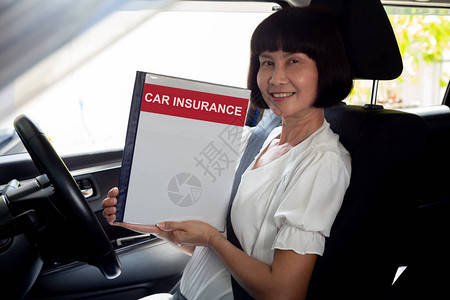 快乐的亚洲高级女拿着汽车保险文件书坐在车里车和保护背景