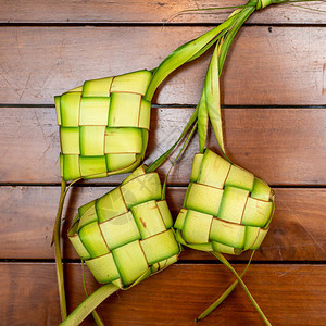 KetupatPouches以木制背景Ketopat是一种用包装在一个钻石形状的圆形棕榈叶袋容器中的背景图片