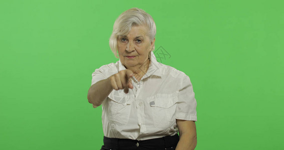 一位老妇人指着镜头微笑一件白衬衫的老俏丽的祖母放置您的徽标或文本色度图片