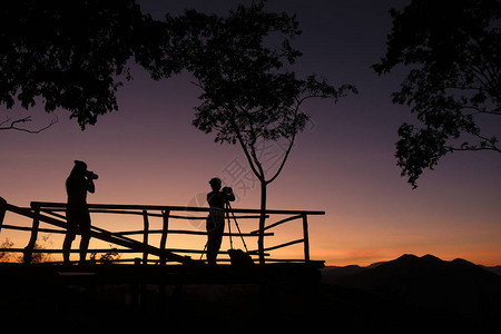 山上的摄影师剪影拍摄日落或日出的风景带相机图片
