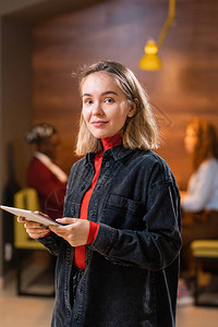 带着移动工具的金发年轻学生在大学咖啡馆面对镜头时站立在镜头前与背景图片