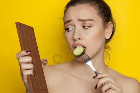 年轻美女吃黄瓜看黄底的朱古力巧克力图片