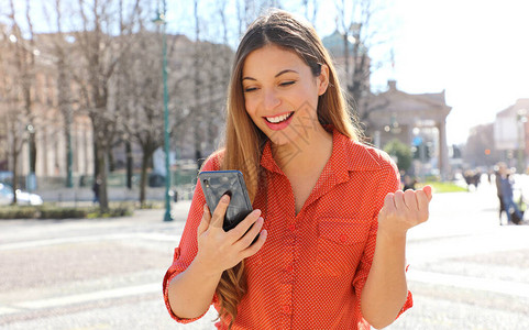 开心兴奋的满意女人拿着智能手机在户外阅读好消息背景图片