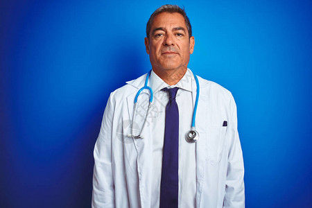 中年帅气的医生男子在孤立的蓝色背景上佩戴听诊器图片素材