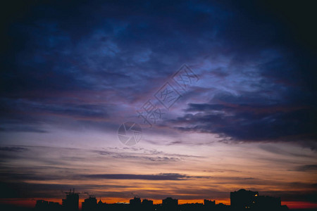 城市景观与生动温暖的黎明令人惊叹的戏剧蓝色紫罗兰色多云的天空在城市建筑的黑暗轮廓之上橙色的阳光阴天中日出的大气背背景图片