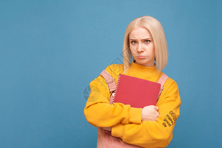 一个女孩风趣学生的肖像站在蓝色背景上图片