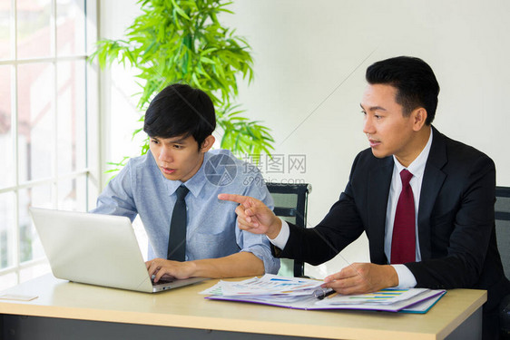 上司在办公室内办公桌前用笔记本电脑向新雇员教图片