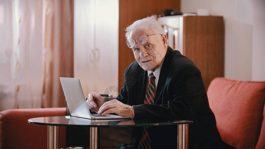 一个戴眼镜的老人坐在笔记本电脑旁边看着摄图片