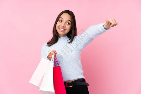 年轻女人拿着购物袋在孤立的粉红背景上买包背景图片