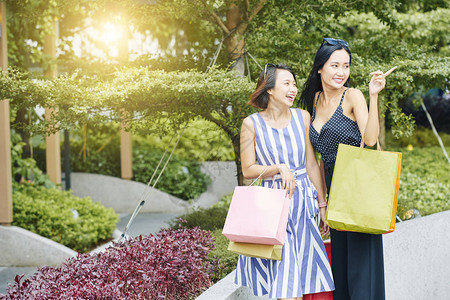 两个亚洲女孩站在购物袋旁看东西图片