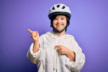 年轻的唐氏综合症骑自行车的女人在紫色背景上戴着安全自行车头盔图片