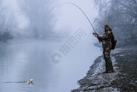 渔民在河岸微雾寒冷的冬季用旋转棒钓鱼轮图片
