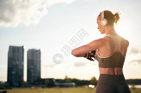 运动服和耳机中强壮的肌肉女后视镜正在吸引智能观察图片