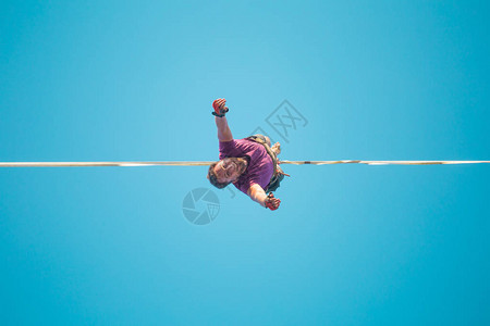 Highliner从下面的蓝天视图垂悬一个人在伸展的吊索上前进走钢丝者的坠落一个人在悬崖边上保背景图片