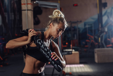 穿着运动服的年轻运动女正在健身房里用肩上的战绳训练功能训练健康的图片