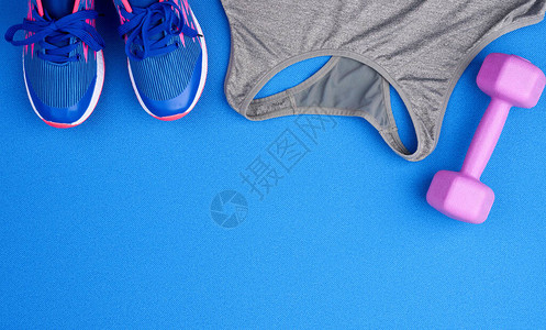 紫色塑料哑铃灰色运动衬衫蓝色背景中的蓝色运动鞋用图片