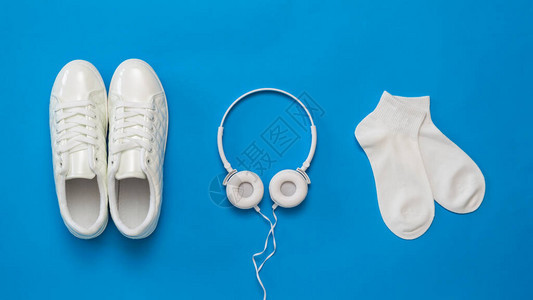 蓝色背景上的白色耳机白色运动鞋和白色袜子颜色趋势健康的生活方式图片