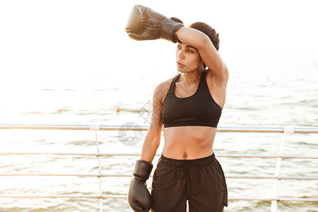 身着运动服装训练的强健漂亮女在海边拳击手套上图片