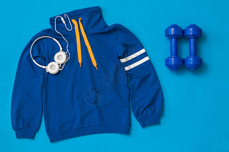 一对蓝色哑铃耳机和蓝色背景上的运动夹克运动图片