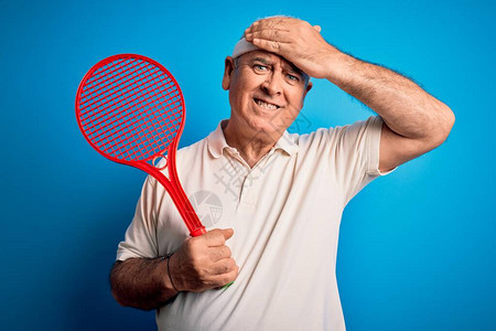 中年男运动员在打网球时用电击横扫孤立的蓝色背景图片
