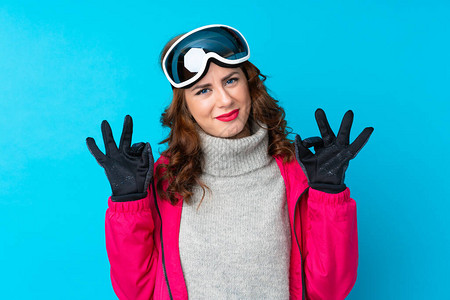 穿着滑雪眼镜的滑雪女人在隔绝的蓝色墙壁上举起手来表图片