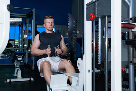年轻男子在健身房用一台电缆重力机训练肩臂和腹部压的肌肉图片