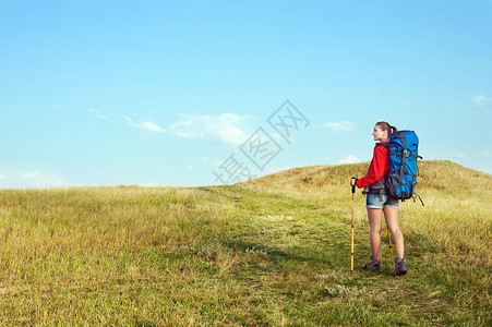 徒步山带着背包和徒步高杆在草地足迹上行走的背景