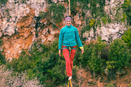 一个女人正沿着一条拉长的吊索行走山中的高线女人抓住了平衡走钢丝者在大背景图片