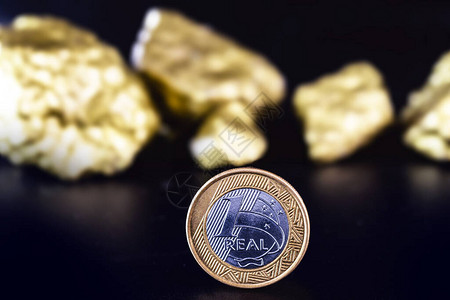 在孤立的黑色背景上的一枚真正的硬币与金块巴西货币升值或巴西黄图片