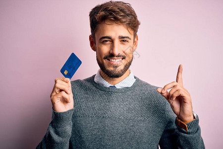 留着胡子的年轻顾客拿着信用卡在粉红色的背景下付款图片